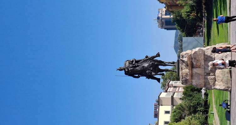 Estatua ecuestre de un héroe nacional sobre un pedestal de piedra alto en una plaza central de la ciudad con cielo azul despejado y edificios alrededor