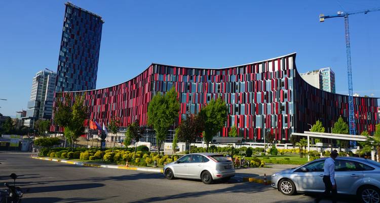 Edificio moderno y curvo con una fachada llamativa en rojo y negro a lo largo de una concurrida calle urbana bajo cielos despejados