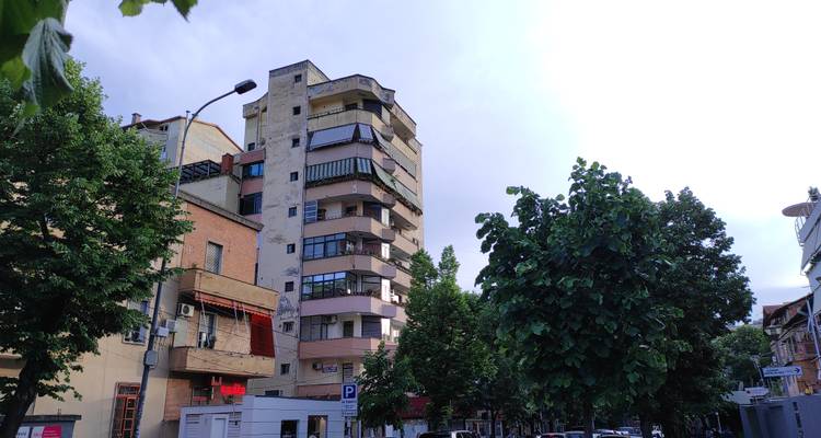 Escena de una calle residencial con edificios de apartamentos de mediana altura, árboles frondosos y cielo nublado