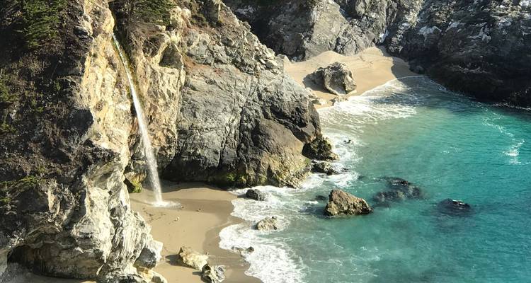McWay Falls plunges from a cliff onto a small sandy cove filled with clear turquoise water along Big Sur’s shoreline.