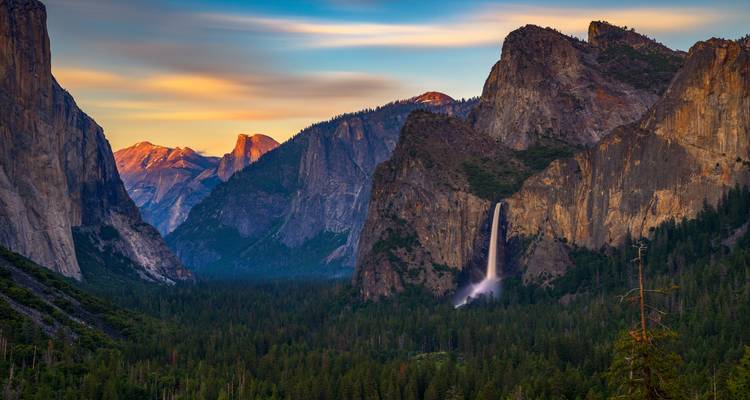 Dramatic sunset light bathes Yosemite’s granite peaks at Tunnel View while Bridalveil Fall cascades into the forested valley.