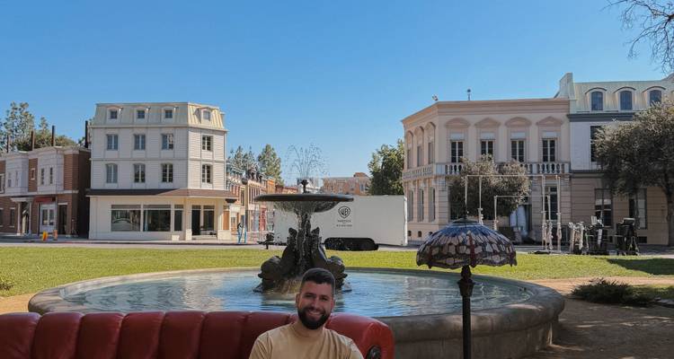 Visiteur souriant assis sur un canapé rouge près d'une fontaine sur un plateau de tournage en studio.