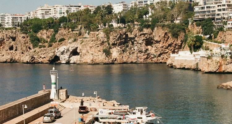 Entrada de la bahía con barcos amarrados bajo acantilados de piedra caliza y el horizonte de la ciudad de Antalya en la parte superior.