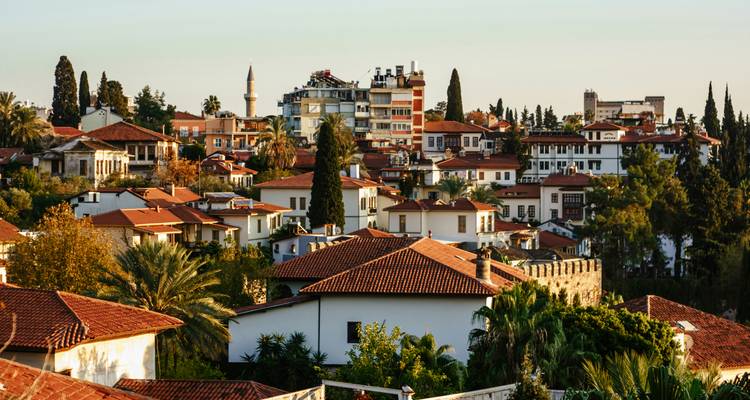 Las casas otomanas con techo de tejas, un minarete y altos cipreses crean un paisaje urbano cálido en la hora dorada.