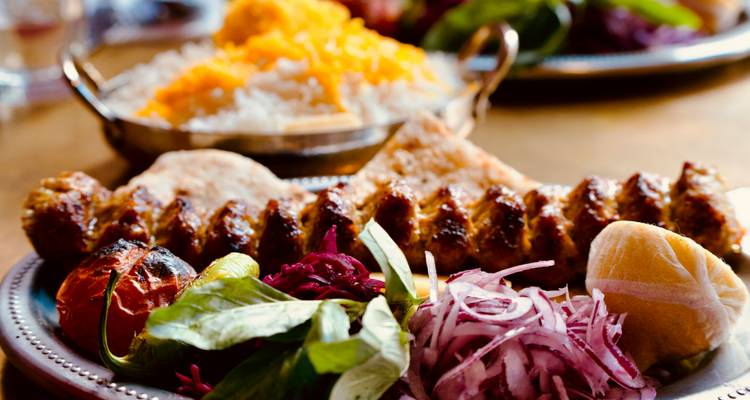 Een close-up van een Turkse kebab spies met rijst en groenten op een metalen schotel.