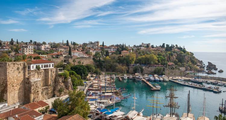 Luchtfoto van Antalya's ommuurde oude binnenstad en drukke jachthaven onder een gestreepte blauwe hemel.