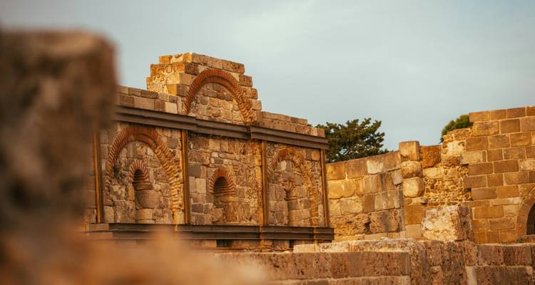 Primer plano de ruinas de piedra iluminadas por el sol con arcos ornamentados y texturas cálidas.