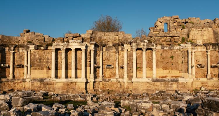 Impresionante estructura antigua con columnas, bloques de piedra iluminados por el sol y ruinas dispersas en primer plano.