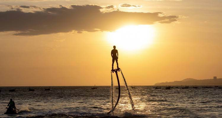 Silueta de un hombre practicando flyboard muy alto sobre el mar durante una puesta de sol dorada y dramática.