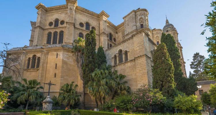 Extérieur ensoleillé de la Cathédrale de Malaga s'élevant au-dessus de jardins luxuriants et de palmiers.