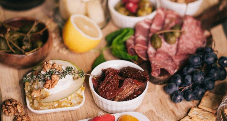 Planche en bois garnie de spécialités méditerranéennes comprenant du fromage, des charcuteries, des olives et du raisin.