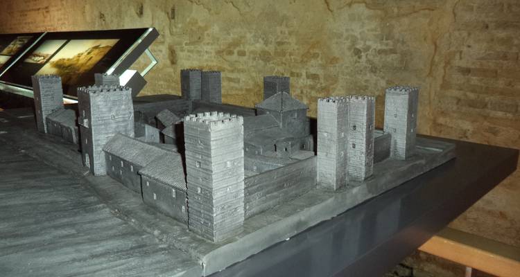 Exposition muséale intérieure d'une maquette de château gris miniature contre un mur en pierre.