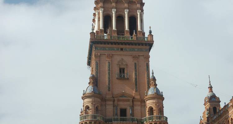 Grande tour ornée de la Plaza de España à Séville se dressant contre un ciel partiellement nuageux.
