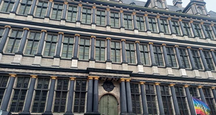 Formal façade with repetitive columned windows and rainbow flag at base.