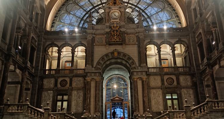 Grand marble hall and staircase of Antwerp Central Station lit by ornate skylight.