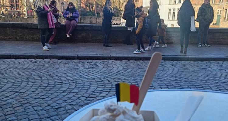 Whipped-cream topped dessert with Belgian flag on outdoor café table overlooking cobbled street.