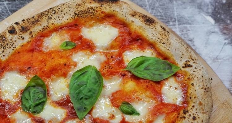 Klassieke margherita pizza met gesmolten mozzarella, tomatensaus en verse basilicumblaadjes op een houten bord.