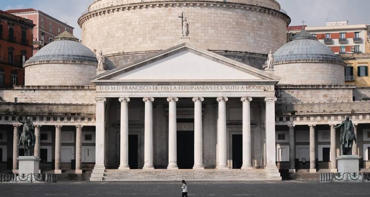 Gevel van de basilica San Francesco di Paola met indrukwekkende zuilen en koepels, een enkele bezoeker die ervoor staat.