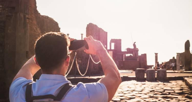 Reiziger die zonnige ruïnes in Pompeï fotografeert met een smartphone, staand op een oude stenen straat.