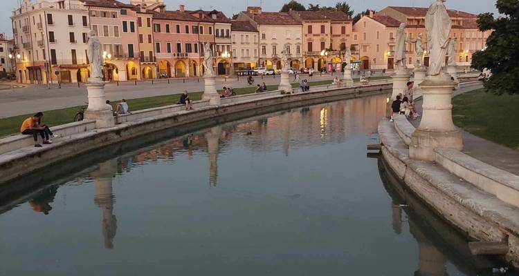 Twilight scene of Padua’s Prato della Valle with statues lining an oval canal reflecting historic buildings.