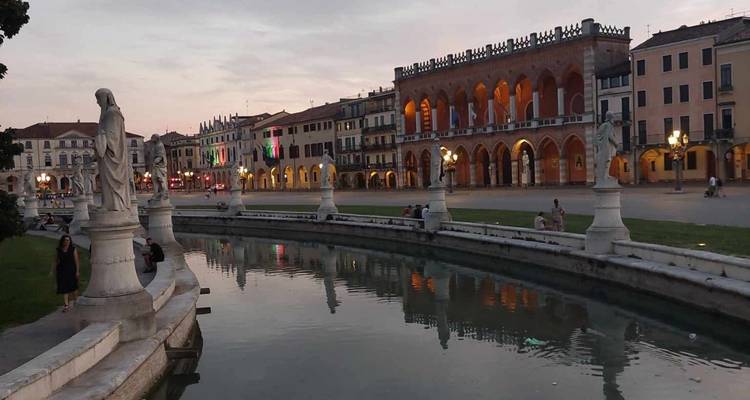 Evening lights illuminate arcaded buildings and statues along the canal in Padua’s Prato della Valle.