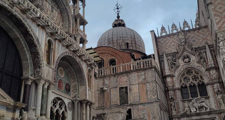 Ornate arches and domes of St Mark’s Basilica rising against a grey sky.
