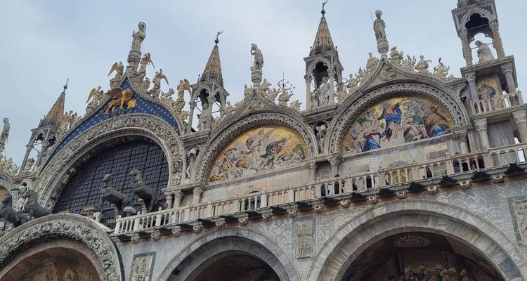 Detailed façade of St Mark’s Basilica with golden mosaics, statues and horses.