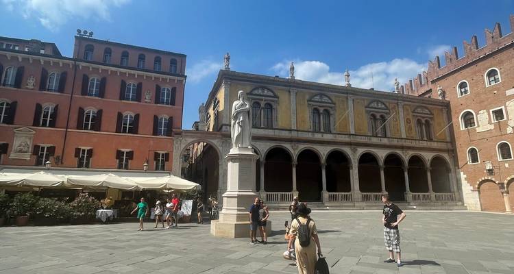 Sunny square in Verona with colourful buildings and Dante statue surrounded by visitors.