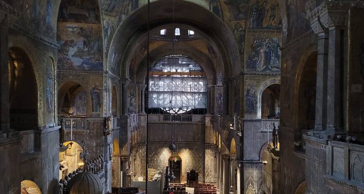 Dimly lit interior of St Mark’s Basilica showcasing mosaics, arches and columns.