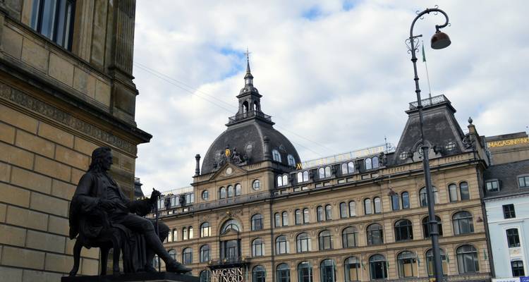 Bâtiment historique du Magasin du Nord avec dôme central et une statue au premier plan sous un ciel partiellement nuageux