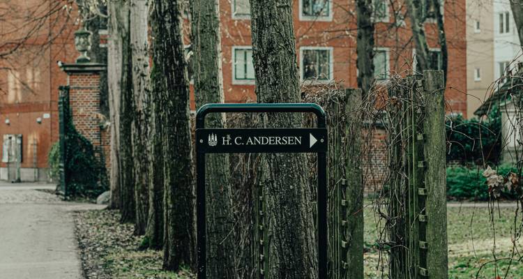 Panneau directionnel pointant vers H. C. Andersen le long d'une allée bordée d'arbres dans un parc urbain