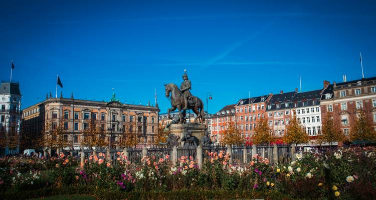 Statue équestre s'élevant au-dessus d'un parterre de fleurs vibrant avec des bâtiments classiques de Copenhague et un ciel bleu dégagé