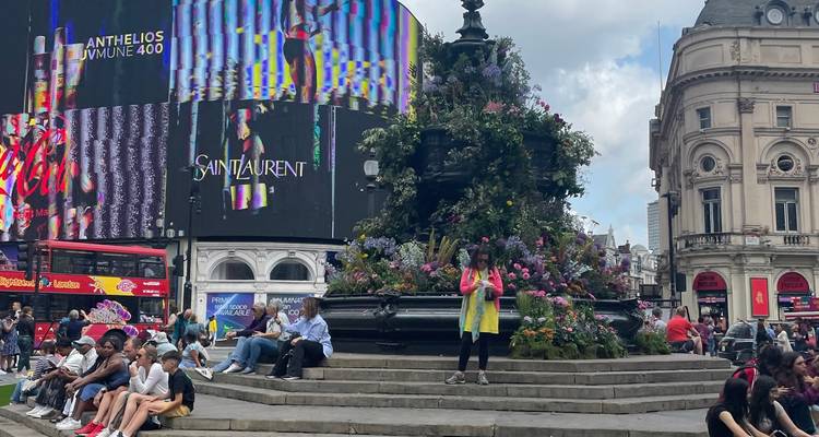 Piccadilly Circus with people sitting around the Eros fountain and large electronic billboards towering overhead
