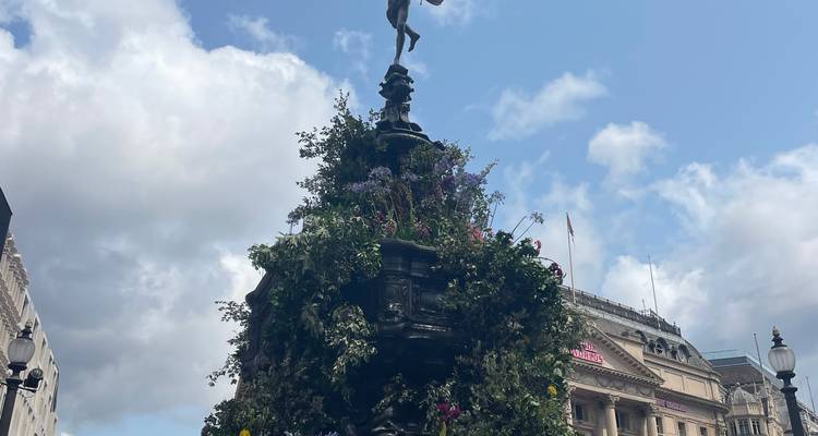Close-up of the ornate Shaftesbury Memorial Fountain adorned with flowers against a blue sky