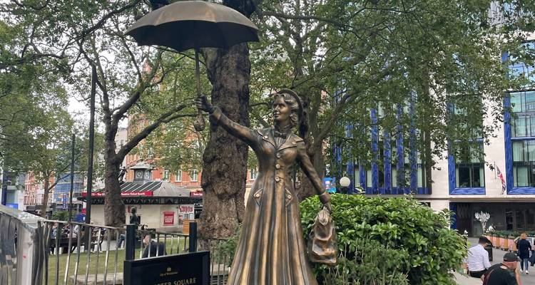 Bronze statue of a woman holding an umbrella in a leafy city square