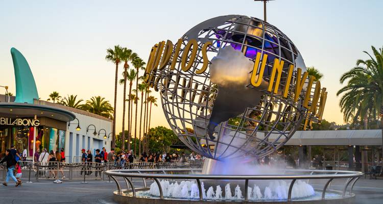 Fontaine iconique du globe Universal Studios rotatif avec palmiers et foules à l'entrée du parc à thème à la lumière chaude du soir