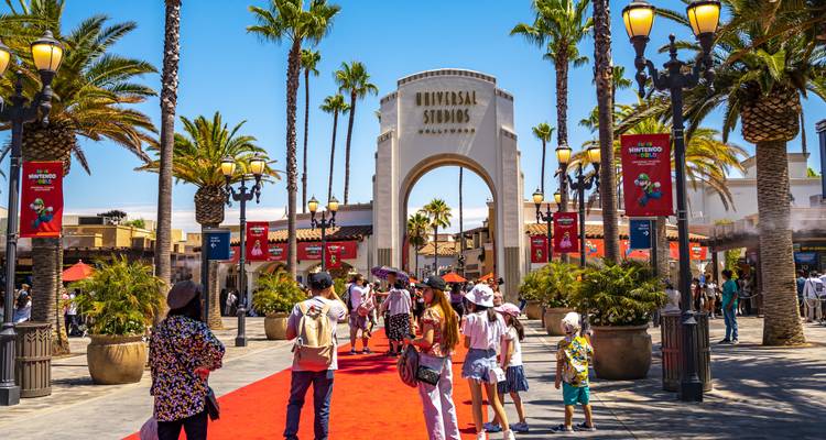Les familles et les enfants marchent sur le tapis rouge en direction de l'entrée voûtée des Universal Studios par une belle journée ensoleillée avec des palmiers.