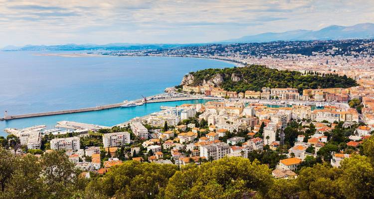 Point de vue panoramique sur Nice avec toits, port, promontoire et montagnes lointaines rencontrant la mer.
