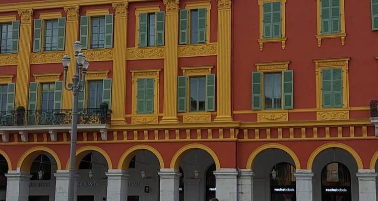 Façade colorée avec des arches, des volets et des colonnes décoratives dans une place méditerranéenne.