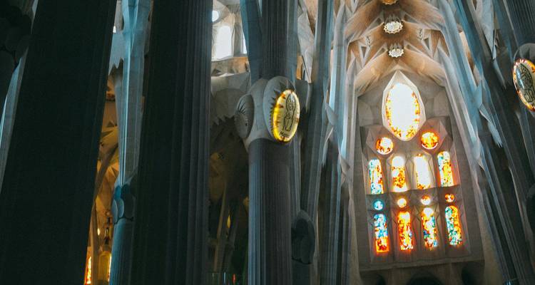 Innenraum der Sagrada Familia mit aufragenden Säulen und farbigen Buntglasfenstern, die Licht in die Basilika werfen