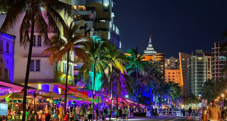 Scène animée nocturne sur Ocean Drive à Miami avec des bâtiments illuminés au néon, des palmiers et des foules