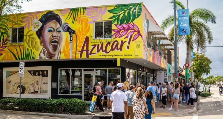 Des files d'attente de visiteurs se forment à l'extérieur d'une colorée boutique de crème glacée à Little Havana, avec une murale affichant « Azucar ! »