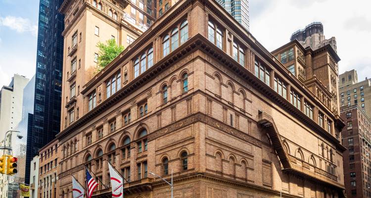Historic red-brick Carnegie Hall stands at a busy Midtown corner with flags flying.
