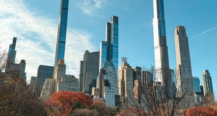 Bright Central Park foliage with soaring Billionaires’ Row skyscrapers under blue sky.