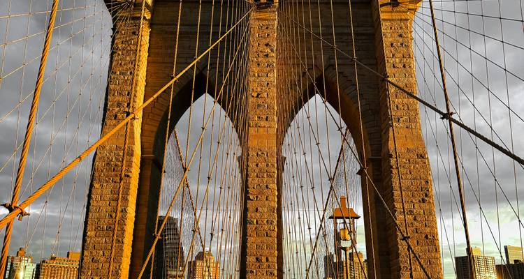 Brooklyn Bridge towers glowing in warm late-day light, framed by its iconic cables.