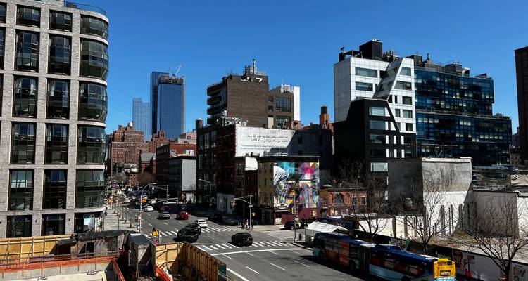 Modern and older buildings line a wide intersection in Chelsea under clear blue sky.