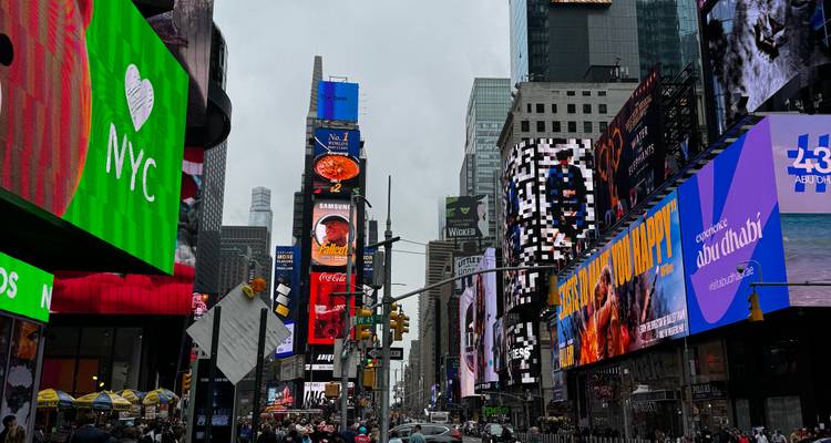Times Square daytime chaos with bright billboards and crowded sidewalks.