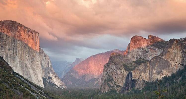 Les falaises de granit de Yosemite rougeoyantes de rose à l'aube sous des nuages dramatiques.