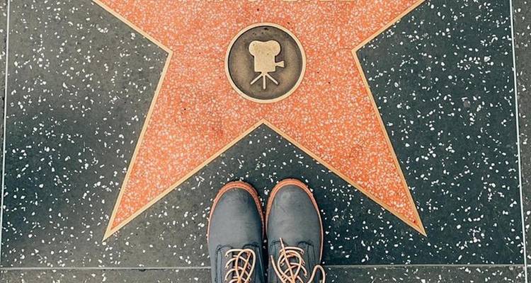 Close-up of boots standing at a blank Hollywood Walk of Fame star on speckled sidewalk.