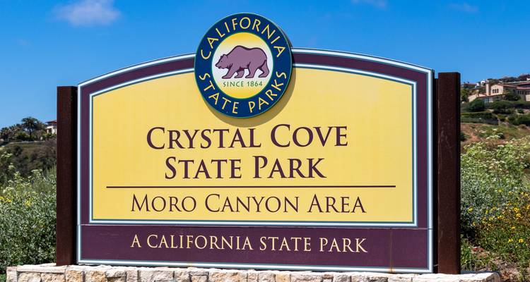 Entrance sign for Crystal Cove State Park set against a clear blue sky and coastal vegetation.